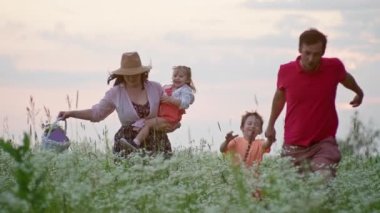 Gün batımında bir tarlada el ele koşan mutlu beyaz bir aile. Çocukların mutluluğu konsepti gülümseme, ailenin yaşam tarzı, ebeveynlerin kızlarıyla oğulları arasındaki ilişki.. 