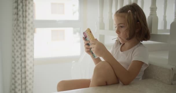 少女は家の階段に座っている間に電話で話している 美しいかわいい子供は スマートフォン上のビデオやソーシャルネットワークを見ています 高品質4K映像 — ストック動画