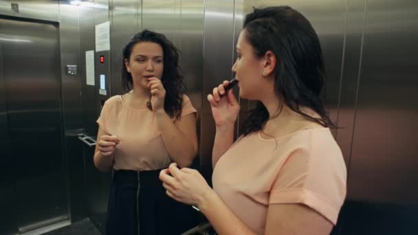 白人女性はエレベーターの鏡の前で口紅で彼女の唇を描きます日付に急いで ドレス姿の美人がパーティーに駆けつける 高品質4K映像 — ストック動画