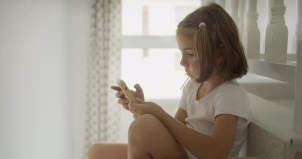両親が家で働いている間 白人の子供は電話にかかっています 時間は友人のいない子供の頃 スマートフォンでゲームやビデオをプレイしました 高品質4K映像 — ストック動画