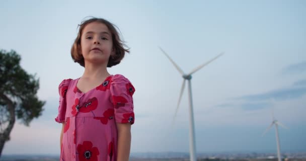ある分野の風力タービンを背景に少女の子供が立っている 風力タービンからの代替電源の実装の自由と環境保護の概念 — ストック動画
