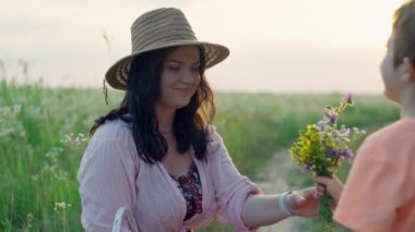 Oğlu annesine bir buket kır çiçeği veriyor, o da ona sarılıyor. Mutlu aile, çocuklar anneye aşık, gülümseme ve şefkat, Anneler Günü. Yüksek kalite 4k görüntü