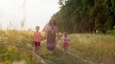 Bir annenin köy yolunda yürüdüğü ve çocuklarını kollarından tuttuğu sihirli bir video. Aile mutluluğu, özgürlük ve barış kavramı, çocuklar ve ebeveynler karşılıklı anlayış 