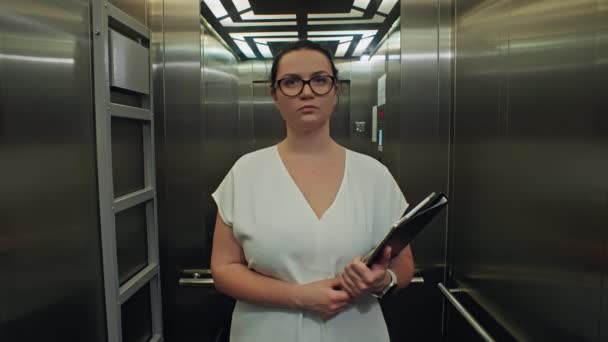 一个商人手里拿着一个文件夹在一幢办公楼里乘坐电梯 一位穿着经典服装的女士在办公室里工作 急于与股东见面 高质量的4K镜头 — 图库视频影像