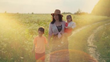 Bir anne, oğlu ve kızıyla birlikte tarlada gülümseyerek yürür. Yaşam tarzı, mutlu aile kavramı, çocuklar için ebeveyn sevgisi. Yüksek kalite 4k görüntü