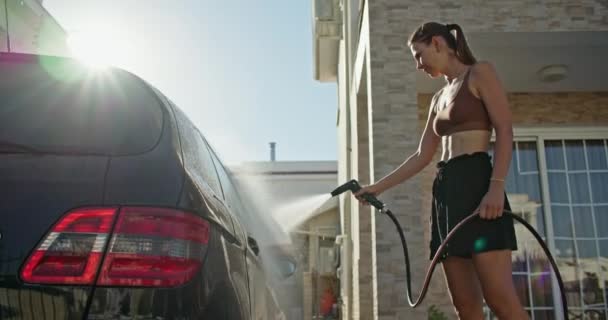 コーカサス人の女性が水ホースで車を洗います 女の子は自宅の庭の汚れから車を掃除する 高品質の4K映像 — ストック動画