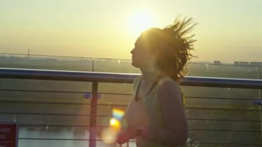 Şafak vakti şehirde koşan sporcu kız. Bir kadın sabah güneşinin altında koşuyor. Aktif bir yaşam tarzı, spor ve spor. Yüksek kalite 4k görüntü