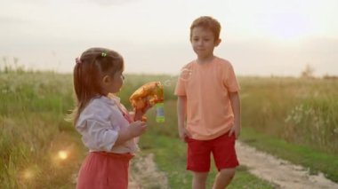 Gülümseyen çocuklar sahaya neşeyle sabun köpüğü fırlatırlar. Tarlada oynayan bir kız ve bir oğlanın eğlencesi. Yüksek kalite 4k görüntü