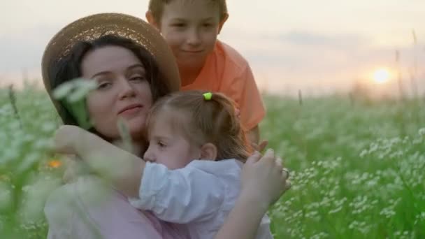畑の草の中に座っている間 息子と娘は母親を抱擁します 子供たちの幸福の概念は笑顔と夢 幸せな家族 母親のライフスタイル 高品質4K映像 — ストック動画
