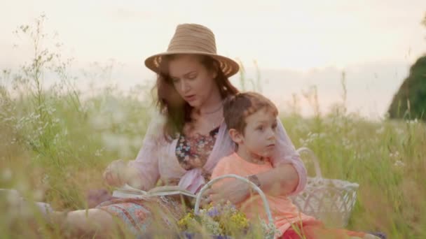 母は息子に草の上に座っている本を読みます 幸せな家族と賢い子供たち 子供の教育の幸福の概念 高品質4K映像 — ストック動画