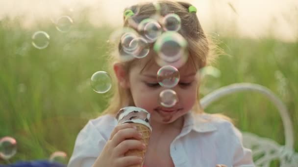 子供の不幸な女の子は公園でアイスクリームを食べるために近づいています 笑顔の子供がピクニックでスイーツを食べる 高品質の4K映像 — ストック動画