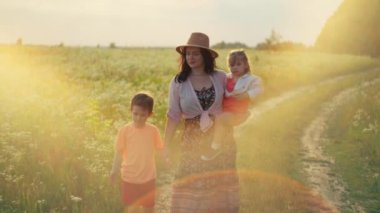 Bir anne, oğlu ve kızıyla birlikte tarlada gülümseyerek yürür. Yaşam tarzı, mutlu aile kavramı, çocuklar için ebeveyn sevgisi. Yüksek kalite 4k görüntü