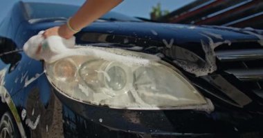Bir kadının araba farını köpüklü bir bez ile yıkarken yakın çekimi. Yüksek kalite 4k görüntü
