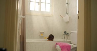 Banyo yaparken bir kız çocuğu oyun oynuyor. Çocuk banyoda banyo yapıyor ve su sıçrıyor. Yüksek kalite 4k görüntü