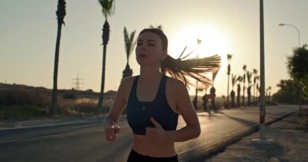 スポーティな女の子は バックグラウンドとしてヤシの木と日没でジョギングを実行します 女性は休暇中にスポーツをする 高品質の4K映像 — ストック動画