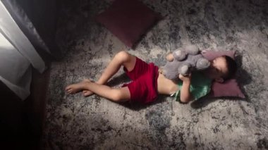 Çocuk evde yerde en sevdiği oyuncağıyla oynuyor. Bir çocuk oyuncak ayıyı kucaklıyor ve onunla konuşmayı öğretiyor. Mutlu çocukluk oyunları konsepti. Yüksek kalite 4k görüntü