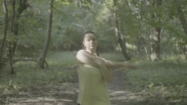 Güzel şişman kız parkta koşmadan önce hazırlanıyor ve ısınıyor. Bir kadın ormanda koşarken kilo verir. Yüksek kalite 4k görüntü