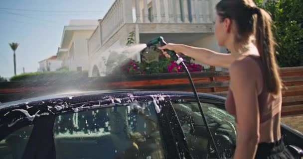 コーカサス人の女性は 洗濯物を持って庭で自宅で車を洗います 女の子は泡にスポンジを浸し 汚れから車をきれいにします 高品質の4K映像 — ストック動画