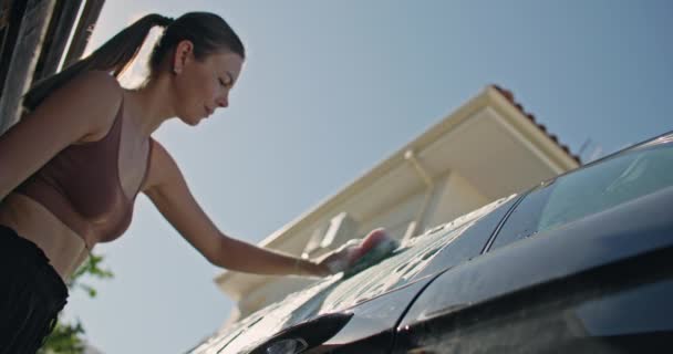 女性は庭の自宅で発泡剤で洗濯物で車を洗います 若い女の子は旅行前に汚れから車の窓をきれいにします 高品質の4K映像 — ストック動画