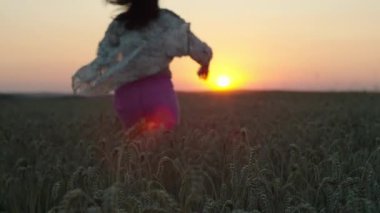 Güzel doğa manzarasında gün batımında buğday tarlasında koşan mutlu kadın. Mutluluk ve özgürlük kavramı, tarım tarlalarında tahıl yetiştirmek. Yüksek kalite 4k görüntü