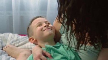 Anne ve oğlu yatak odasında oynaşıp eğleniyorlar. Bir kadın bir çocuğa sarılır, aile bakımı ve sevgi kavramı, çocuklar gülümser ve sevinir. Yüksek kalite 4k görüntü