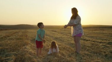 Neşeli anne ve çocuklar gün batımında buğday tarlasında samanı yokuş yukarı atıyorlar. Mutlu aile birlikte oynaşıyor, aşk kavramı birlikte zaman geçirmenin zevki. Yüksek kalite 4k görüntü