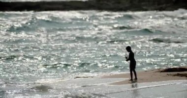 Deniz kıyısındaki bir çocuğun silueti. Güzel dalgalar kumlu bir kumsalda yavaş çekim video eğlencesi ve turizmle çarpışıyor. Yüksek kalite 4k görüntü