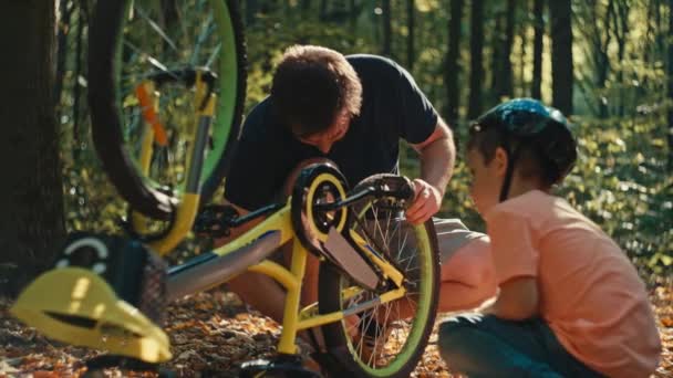 爸爸教他的儿子怎样正确修理自行车 一个骑自行车带着孩子在森林里骑车的男人 亲子关系和快乐童年的概念 高质量的4K镜头 — 图库视频影像