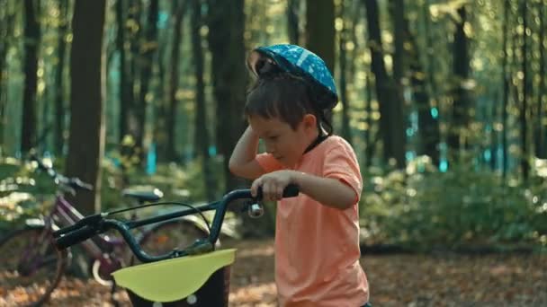一个男孩子戴上头盔 在公园里骑自行车 童年的快乐时光骑自行车在森林里的小径上 高质量的4K镜头 — 图库视频影像