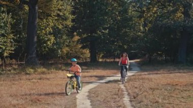 Anne ve oğlu parkta bisiklet sürerler. Mutlu bir aile hafta sonunu aktif olarak birlikte geçirir. Mutlu bir yaşam tarzı. Yüksek kalite 4k görüntü
