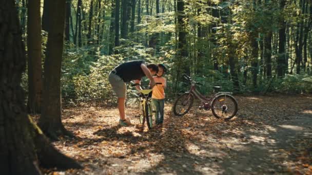 一对父子正在森林里修理一辆自行车 与父母和孩子一起在大自然中度过的积极的娱乐时间 一个男人教一个男孩子修理东西 高质量的4K镜头 — 图库视频影像