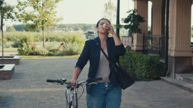 Bir kadın ofise bisikletle gider ve sabah kahvesini içer. Gülümseyen bir kız iş merkezine buluşmaya gider. Yüksek kalite 4k görüntü