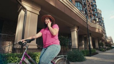 Bisikletli bir kız şehir manzarasında telefonla mesajlaşıyor. Bir kadın bisiklet sürerken akıllı telefona bakar. Yüksek kalite 4k görüntü