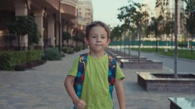 Sırt çantalı mutlu bir çocuk okula gider. Bir okul çocuğu, şehir manzarasında sınıftaki derslere gülümseyerek koşar. Yüksek kalite 4k görüntü