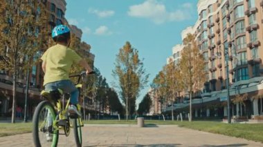 Kasklı bir çocuk güvenli bir şekilde bisiklete biner. Çocuk aktif olarak şehir manzarasında oynuyor ve eğleniyor. Yüksek kalite 4k görüntü