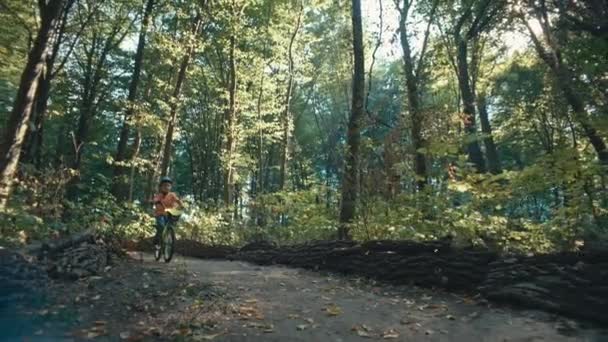 ヘルメットに乗っている白人少年が森で自転車に乗っている 子供は公園で自転車に乗っているときに楽しんで遊んでいます 高品質の4K映像 — ストック動画