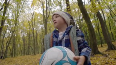 Mutlu bir çocuk sonbahar parkında bir topla oynar. Sarı yaprak mevsiminde dışarıda futbol oynayan gülümseyen çocuk. Yüksek kalite 4k görüntü