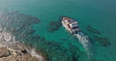 Mavi denizin dalgaları üzerinde kayalıklarda yüzen bir motorlu teknenin hava görüntüsü. Okyanusun güzel manzarası ve bir tekne. Yüksek kalite 4k görüntü