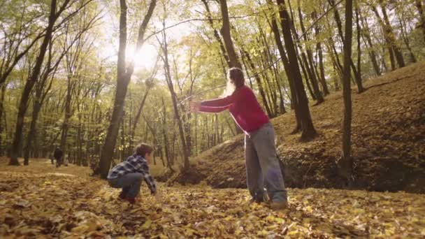 母親と息子は 秋の森で散歩中に黄色い葉を投げるのを楽しんでいる 子供たちと一緒に笑顔の家族 マザーリー 高品質の4K映像 — ストック動画