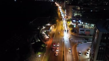 Gece şehrinin hava manzarası, yollarda trafik var. Şehir manzarasında araba farlarının ışığı ve yollardaki gece lambaları. Yüksek kalite 4k görüntü