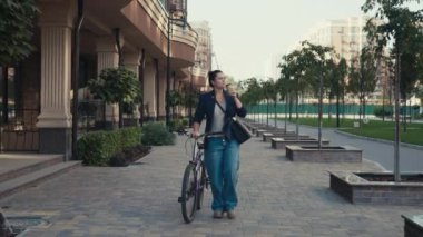 Bir kadın şehir manzarasında bisikletle yürürken işten önce kahvesini bitirir. Bir iş kadını iş merkezinin ofisine bisikletle koşuyor. Yüksek kalite 4k görüntü