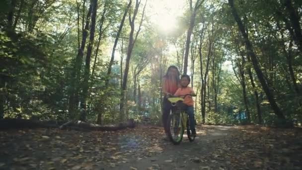 母親は子供が公園で自転車に乗ることを学ぶのを助けます 両親と息子は積極的かつ陽気な時間を過ごしています 高品質の4K映像 — ストック動画