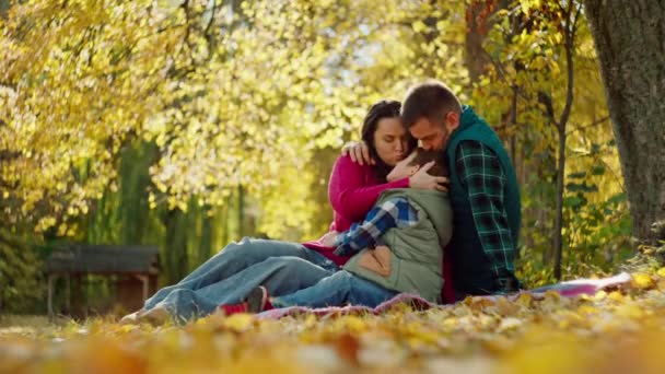コカシア人の家族は秋の公園で黄色い葉の上に眠っている ハッピーな両親は息子を抱きしめ 愛の暖かさの笑顔と秋の季節をコンセプトにしています 高品質の4K映像 — ストック動画