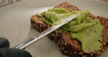 Avokado tostu hazırlayan bir şefin makro yavaş çekim videosu. Avokado ekmeğini bıçakla yaymak. Yüksek kalite 4k görüntü