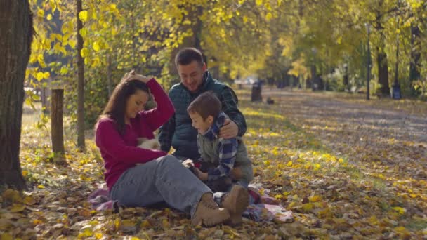 ピクニックで犬と一緒に秋の森で幸せな家族 子供と両親は公園でペットと遊び 笑顔で楽しんでいます 高品質の4K映像 — ストック動画