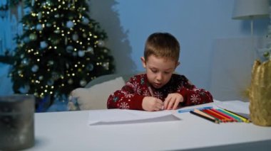 Çocuk evdeki Noel Baba 'ya bir mektup yazıyor. Mutlu bir çocuk, bir kağıt parçasına kalemle yazarak Noel 'e şenlikli bir ortamda hazırlanıyor. Yüksek kalite 4k görüntü