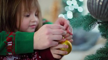 Bir anne kızının Noel ağacına bir süs asmasına yardım eder. Neşeli bir Noel havası, çocuklu mutlu bir aile bayram için hazırlanıyor. Yüksek kalite 4k görüntü