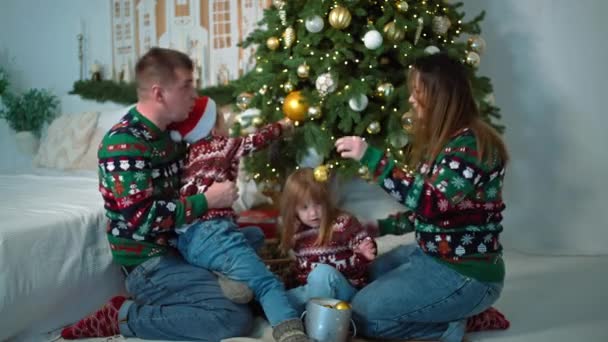 幸せな家族がクリスマスツリーの近くに座って 新年の装飾を見ています 子供と両親は休日のために準備し 笑顔を一緒にします 高品質の4K映像 — ストック動画