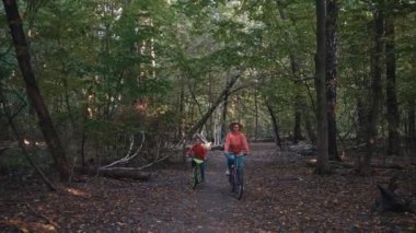 Anne ve oğlu parkta bisiklet sürüyorlar. Aile birlikte zaman geçirir. Bisiklet sürerken rahatlar, eğlenir ve gülümser. Yüksek kalite 4k görüntü