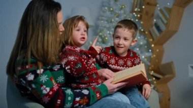 Bir anne dekore edilmiş bir odada çocuklara bir Noel hikayesi okur. Mutlu bir aile tatil ve hediyeler için hazırlanıyor. Yüksek kalite 4k görüntü